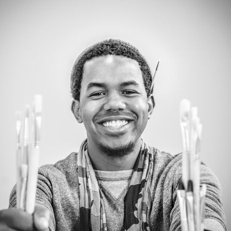 Man holding paintbrushes smiles at camera