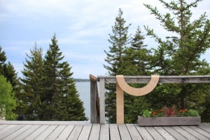 Curved wooden artwork, draped over a railing with pine trees in the distance