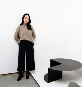 Female standing with black sculptural table against white wall