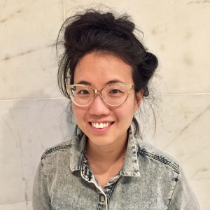 Headshot of a woman with dark hair, clear frame glasses, wearing and acid wash denim shirt