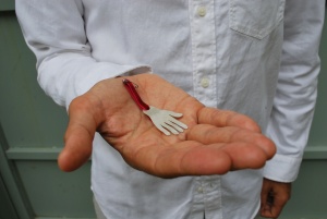 A person's hand holding a silver hand shaped medal with a red ribbon