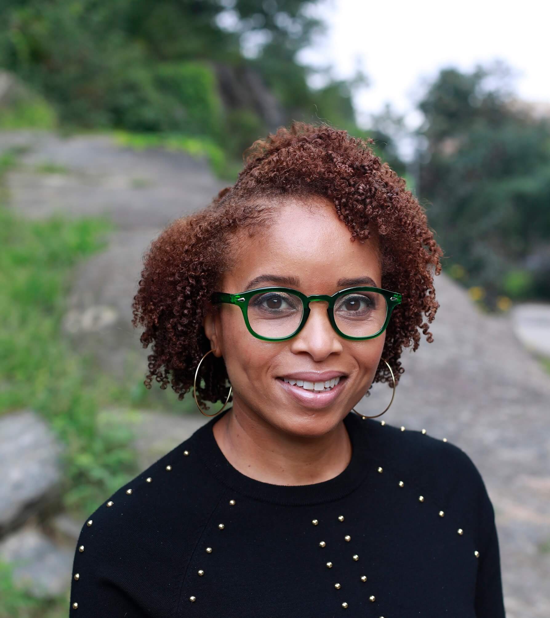 Headshot of a Black woman with gree glasses in a black crewneck sweater.