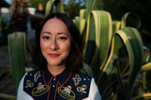 headshot of a woman with dark hair and bright lipstick, with plants in the background