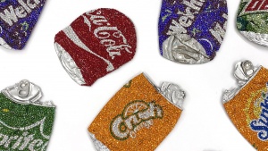 Close up on several pop cans smashed flat, their iconic designs made into a bejeweled surface