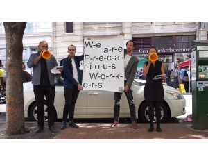 Four people holding up a white sign with black text that reads "we are precarious workers"