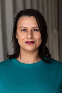 A person with shoulder-length brown hair wearing a teal sweater from the shoulders up.