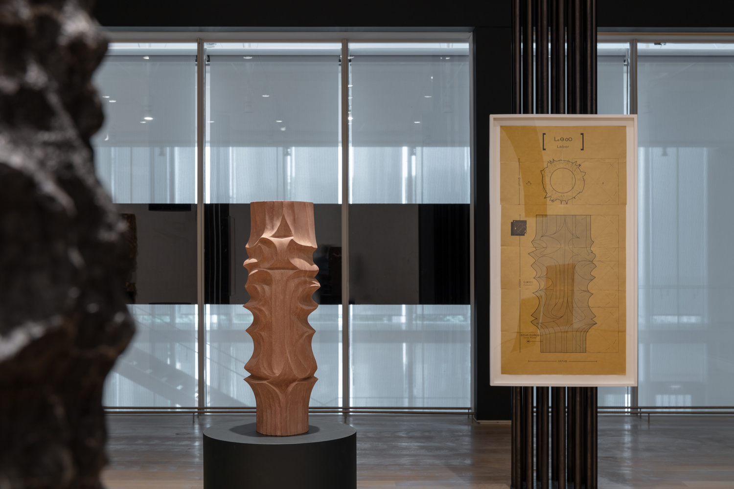 An exhibition view featuring sculpture and two-dimensional work in a glass room. 